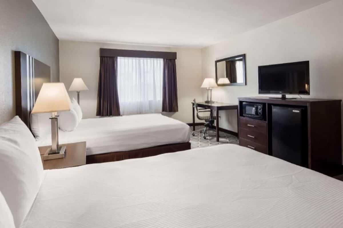 A hotel room with two beds, a desk, a television, and a minibar.