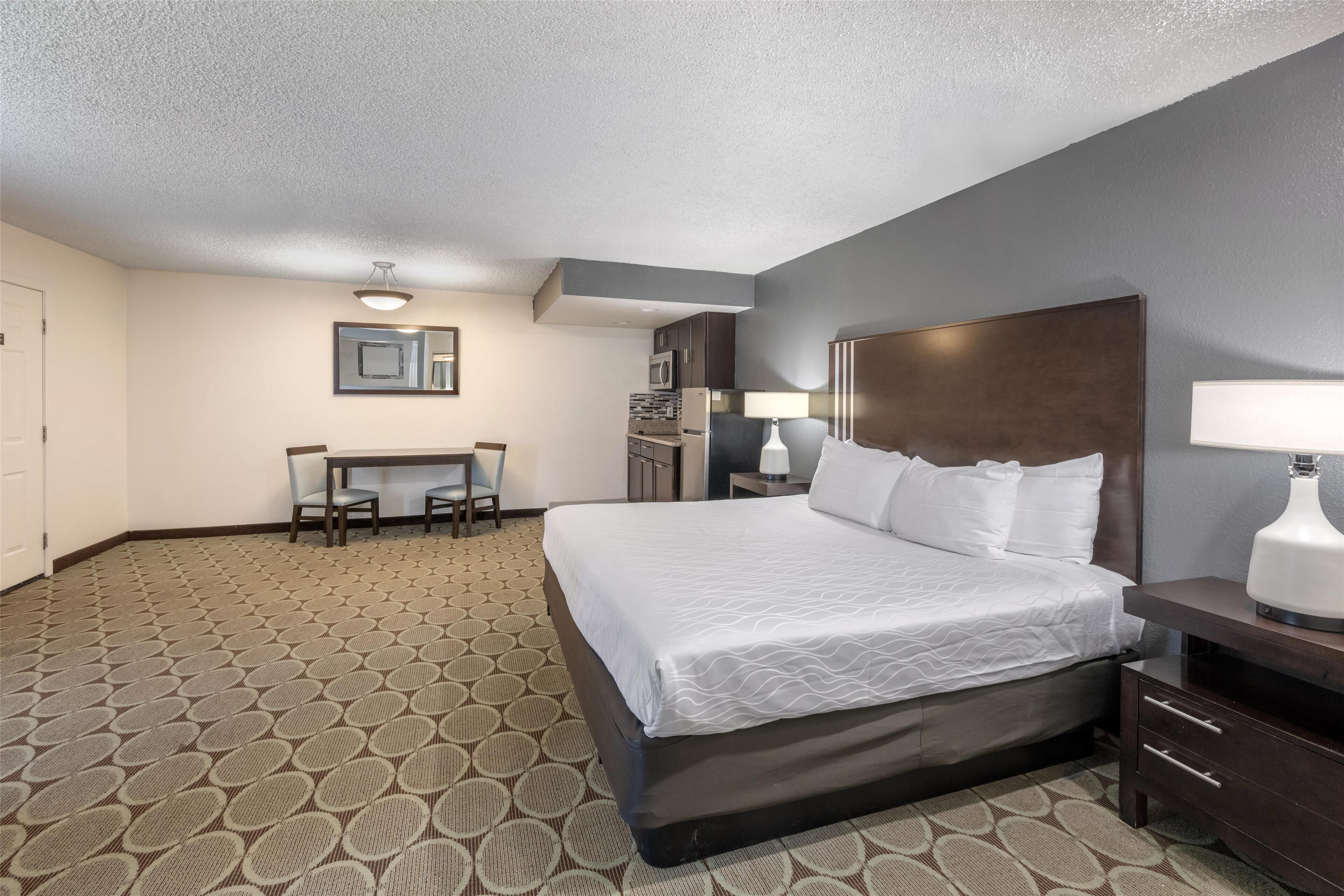 Una habitación de hotel con una cama grande, un escritorio con dos sillas, un microondas y un refrigerador.
