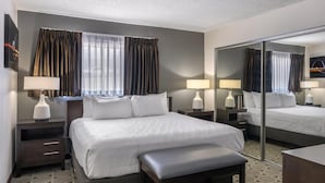 Habitación de hotel con una cama grande, dos mesitas de noche con lámparas, un banco, un espejo y una alfombra estampada.