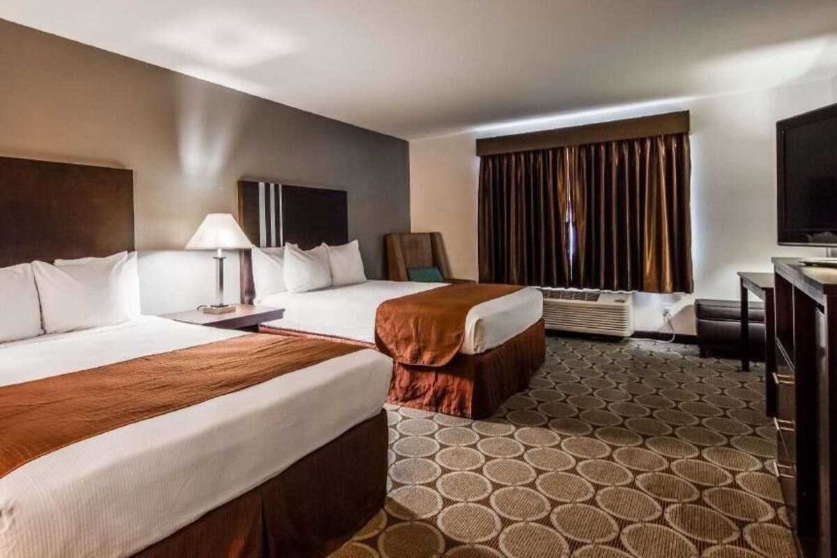 A hotel room with two beds, a desk, a TV, and a window with curtains.