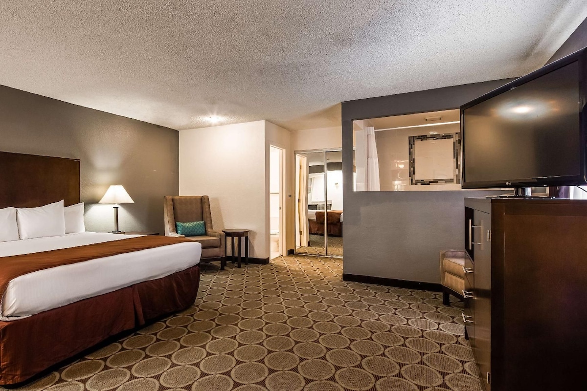 A hotel room with a large bed, a desk, a chair, a television, and a bathroom visible through an open door.