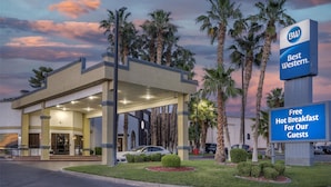 Un hotel con entrada cubierta, palmeras y un letrero que ofrece desayuno caliente gratuito para los huéspedes.