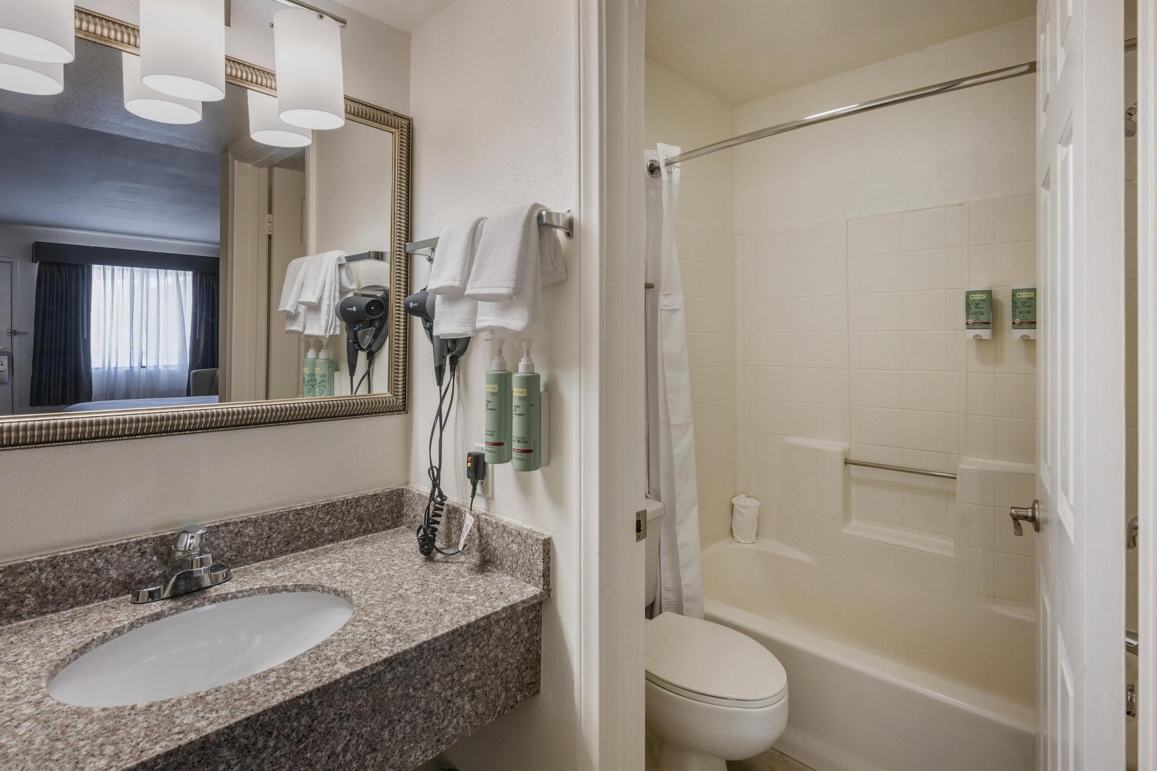 Un baño con lavamanos de granito, un espejo, secador de pelo y zona de ducha.