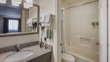 Un baño con lavamanos de granito, un espejo, secador de pelo y zona de ducha.