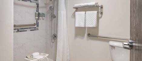A bathroom with a shower, toilet, and a small bench with towels.