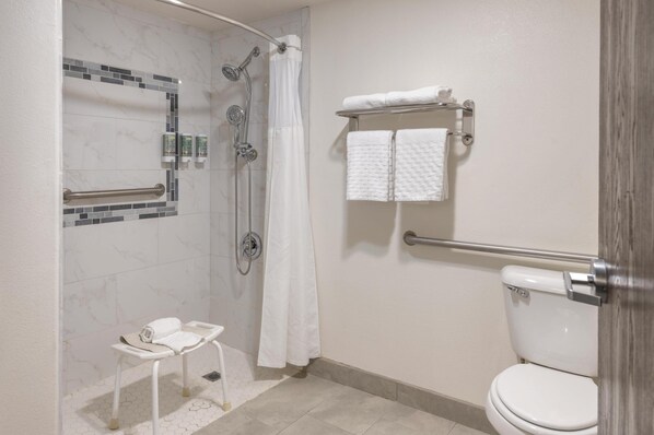 Une salle de bain avec une douche, des toilettes et un petit banc où sont posées des serviettes.