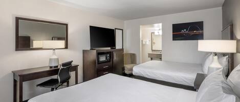 A hotel room with two beds, a desk with a TV, a chair, a microwave, and a mirror.