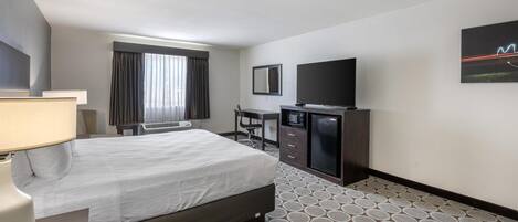 A hotel room with a bed, desk, TV, and a patterned carpet.
