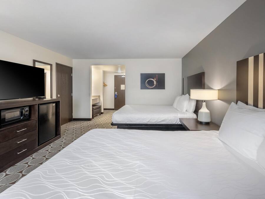 A hotel room with two beds, a TV, a desk with a lamp, and a microwave.