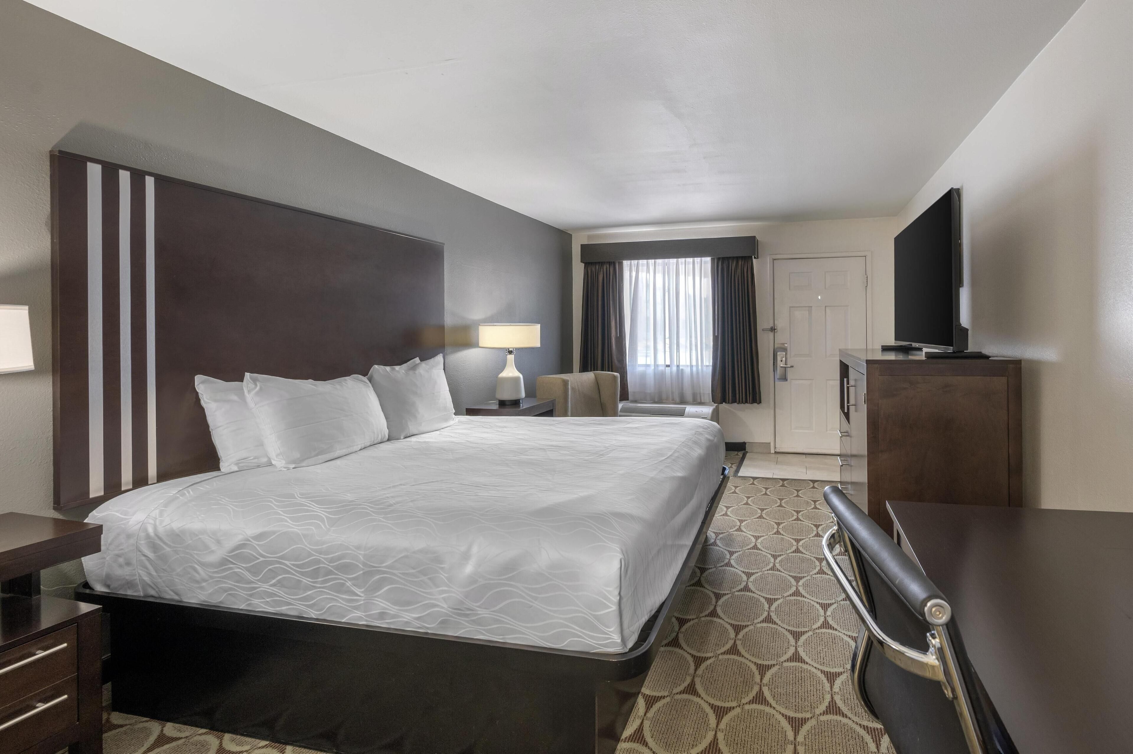 A hotel room with a large bed, a desk, a chair, a television, and a wardrobe.