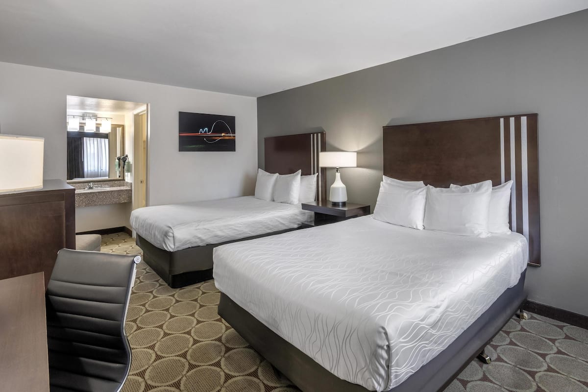 A hotel room with two beds, a desk, a chair, a mirror, and a wall-mounted TV.