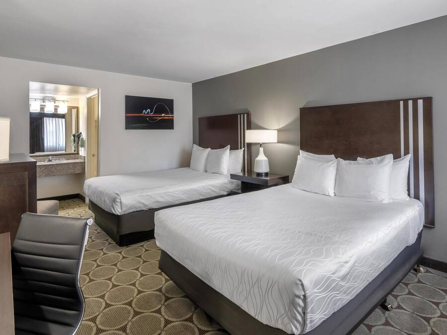 A hotel room with two beds, a desk, a chair, a mirror, and a wall-mounted TV.