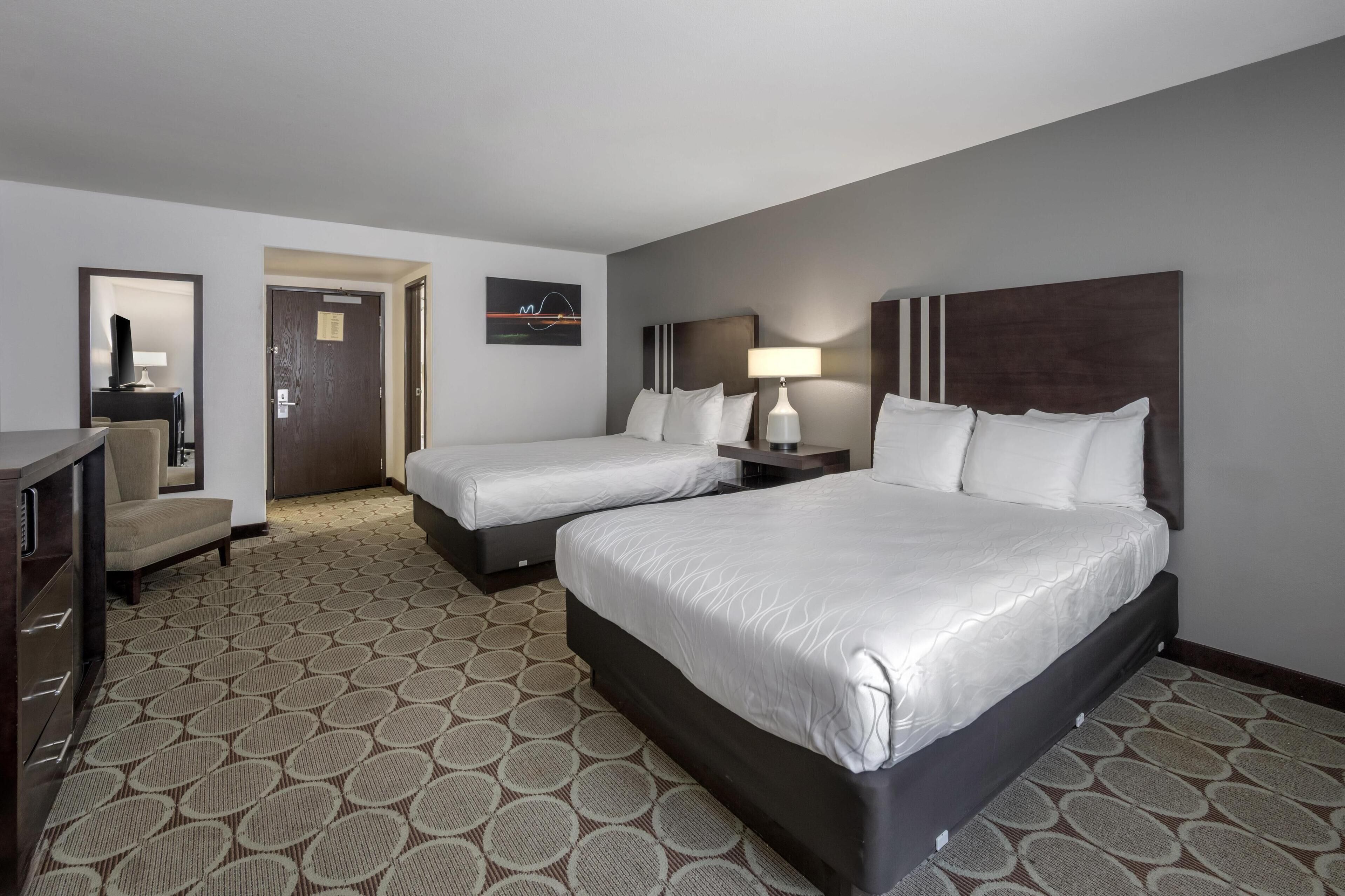A hotel room with two beds, a desk, a chair, and a TV.