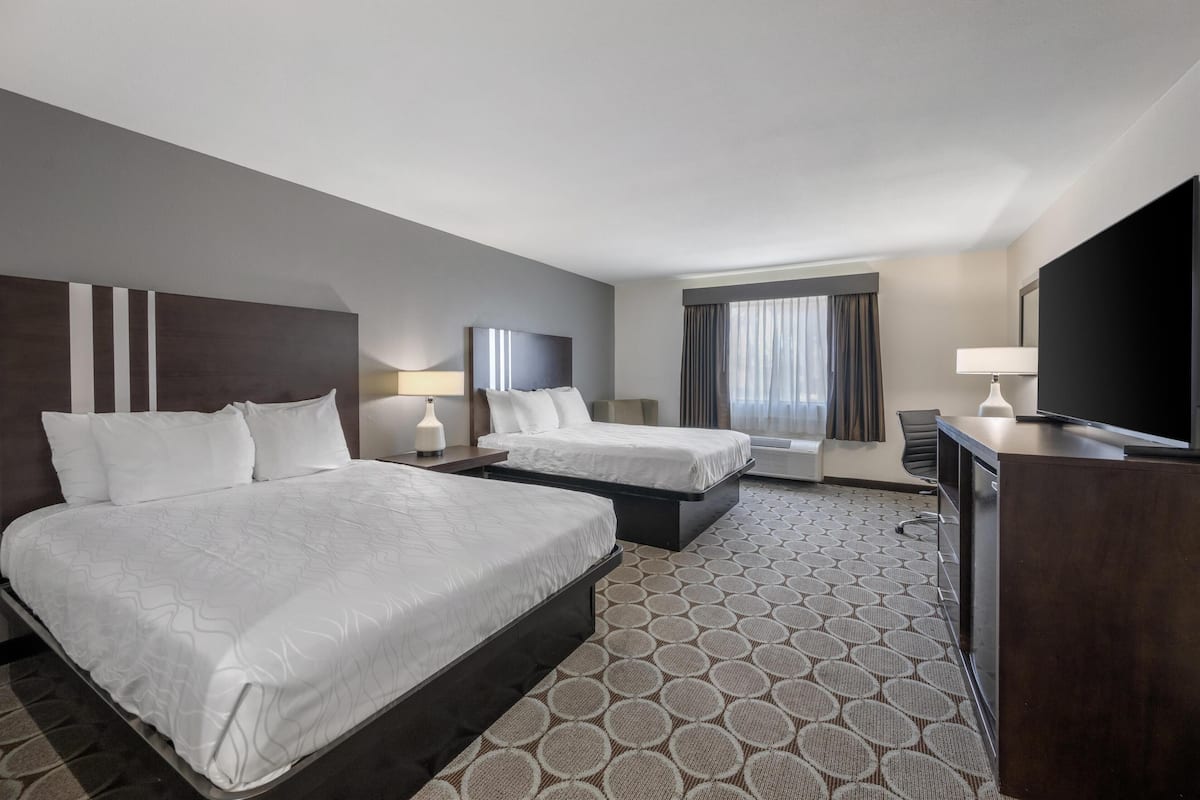 A hotel room with two beds, a desk, a TV, and a window with curtains.
