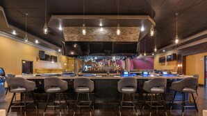 Una zona de bar con varios taburetes, una barra central y lámparas colgantes.