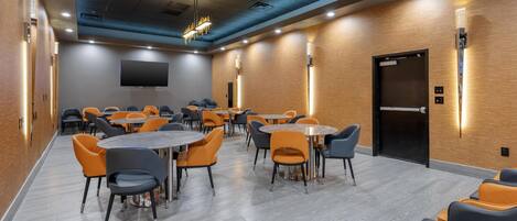A modern conference room with round tables and chairs, a flat-screen TV, and a wooden accent wall.