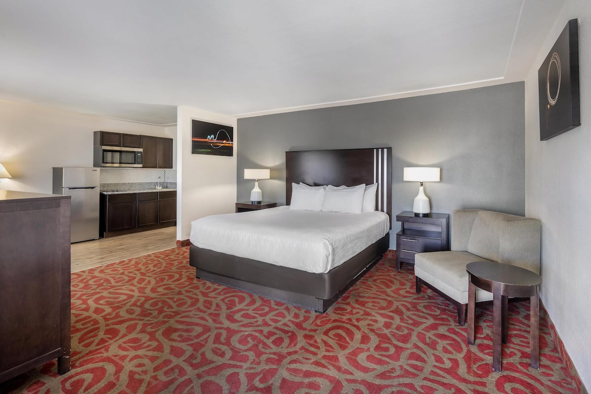 A hotel room with a bed, bedside tables, a desk, and a kitchenette.