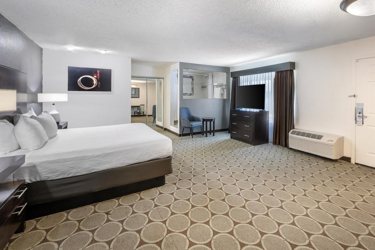 A hotel room with a bed, a desk, a chair, a TV, and a bathroom visible through an open door.