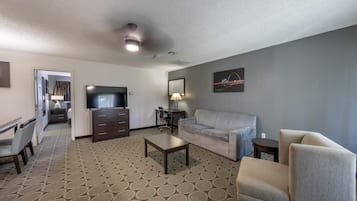 Habitación de hotel con sofá, sillón, televisión, escritorio y alfombra estampada.