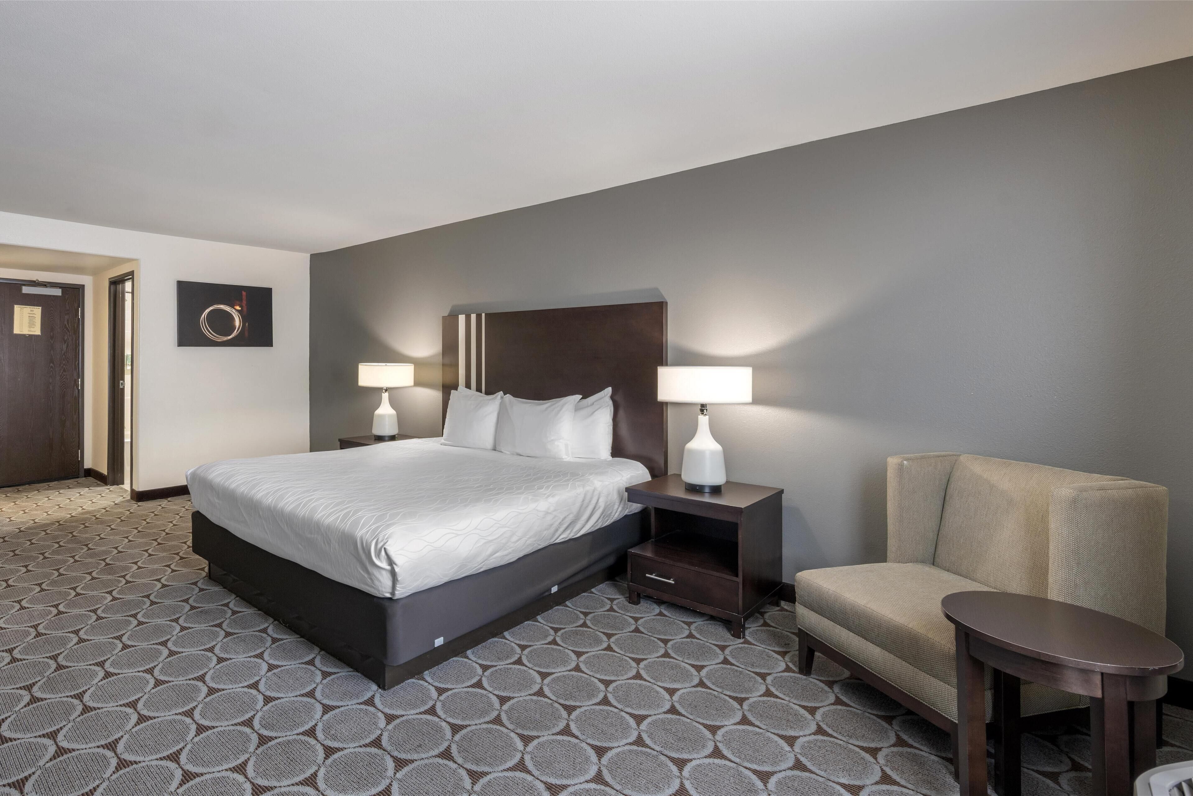 A hotel room with a large bed, two bedside tables with lamps, a small armchair, and a round table.