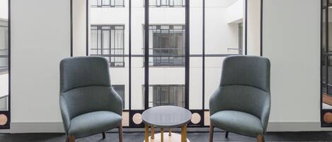 A room with two grey armchairs, a round wooden table, and a patterned floor.