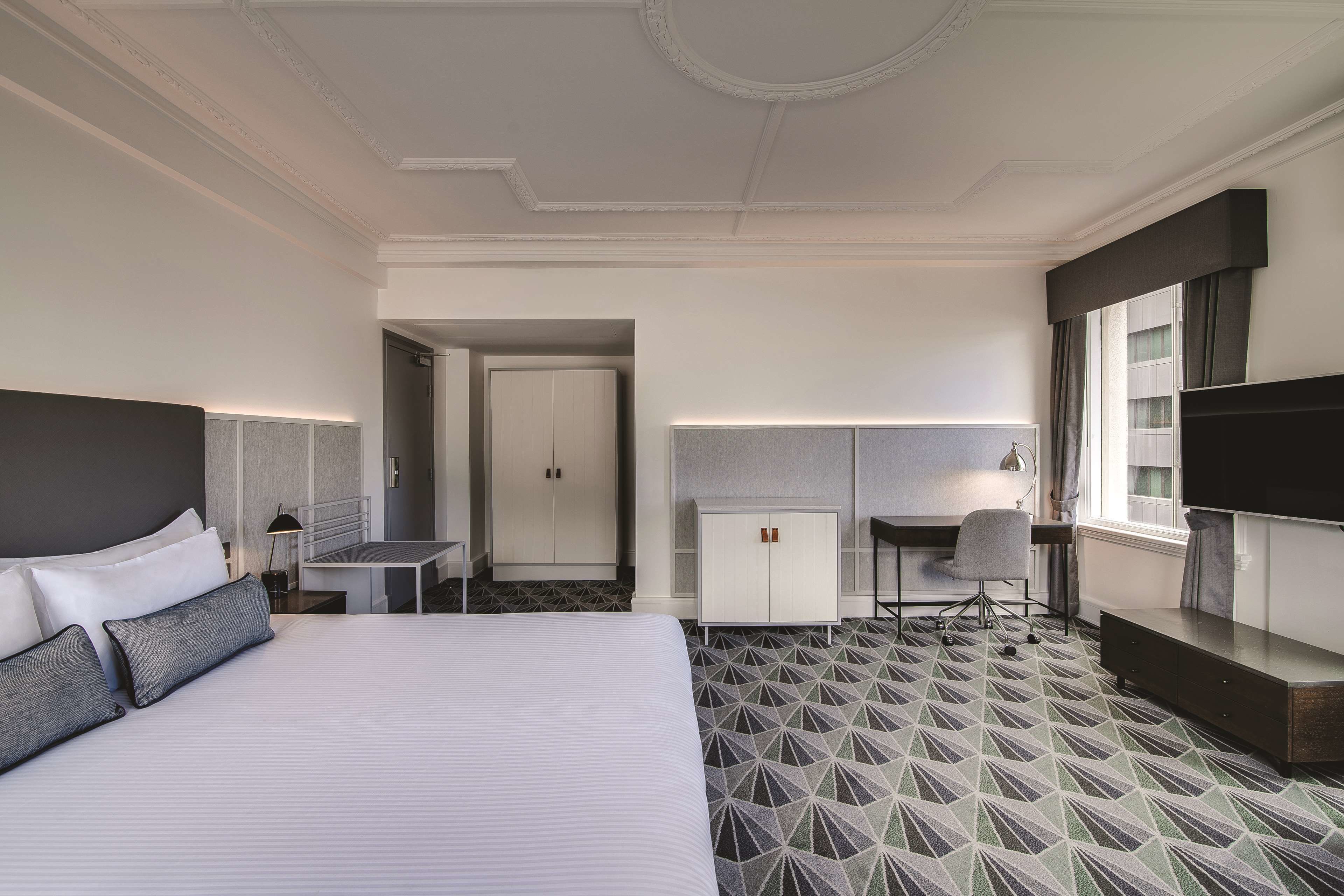 A hotel room with a large bed, a desk, a wardrobe, and a TV.