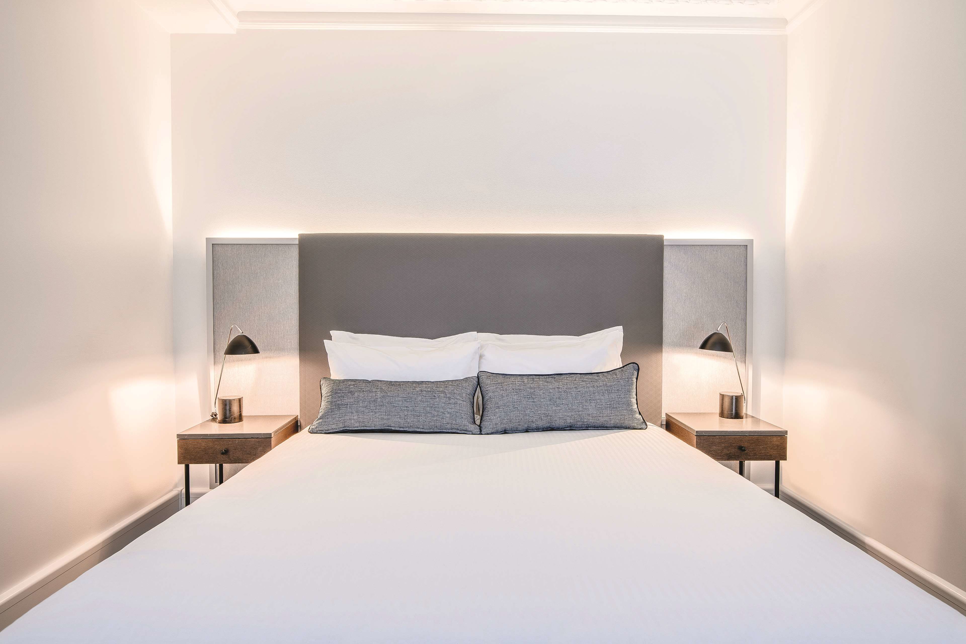 A neatly made bed with white linens, two bedside tables with lamps, and a large headboard.