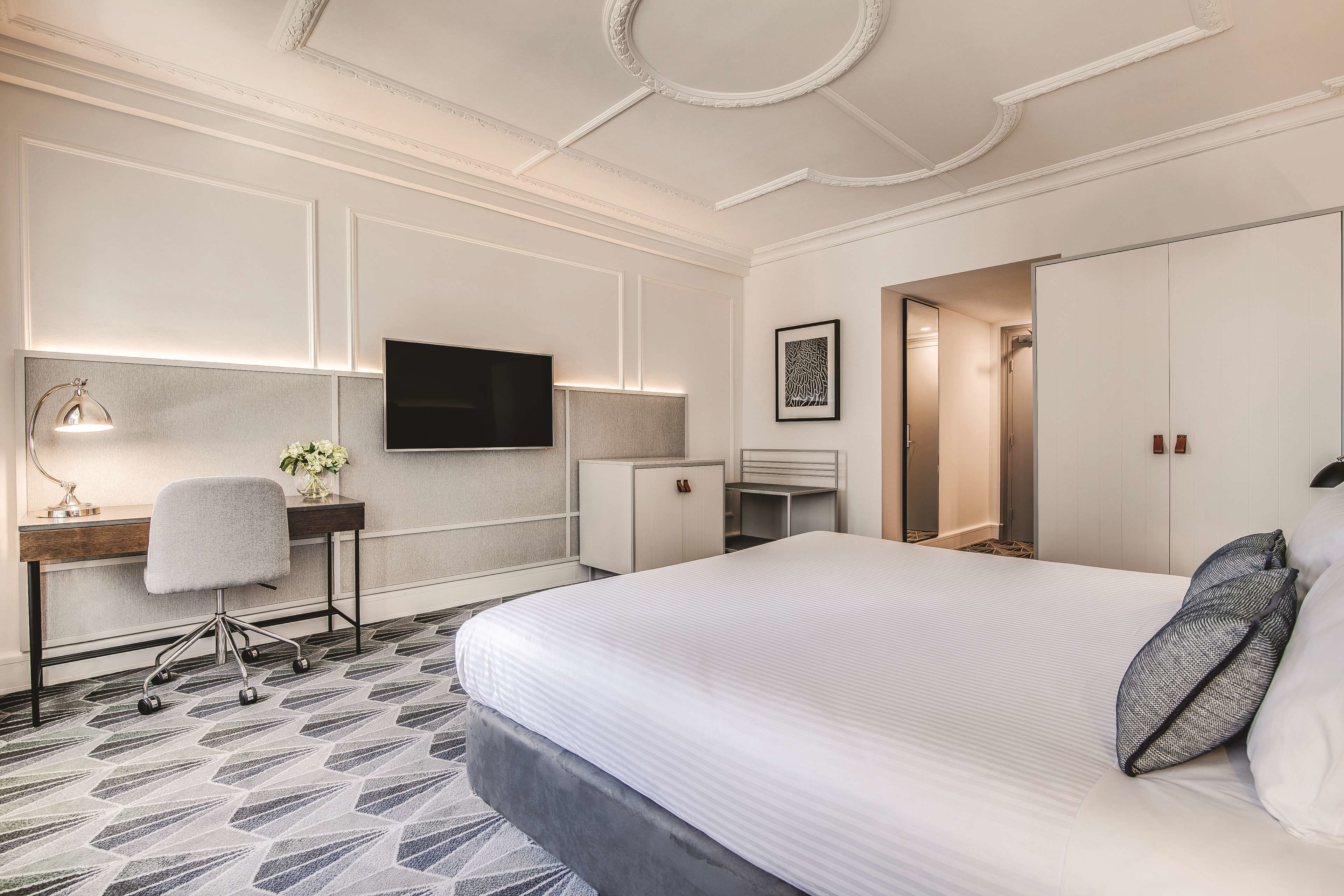 Una habitación de hotel con una cama grande, un escritorio con silla, un televisor montado en la pared y un armario.