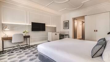 Una habitación de hotel con una cama grande, un escritorio con silla, un televisor montado en la pared y un armario.