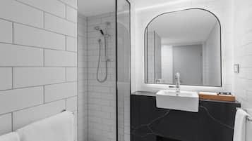 A modern bathroom with white tiled walls, a glass shower enclosure, a black marble sink vanity, and a large mirror.