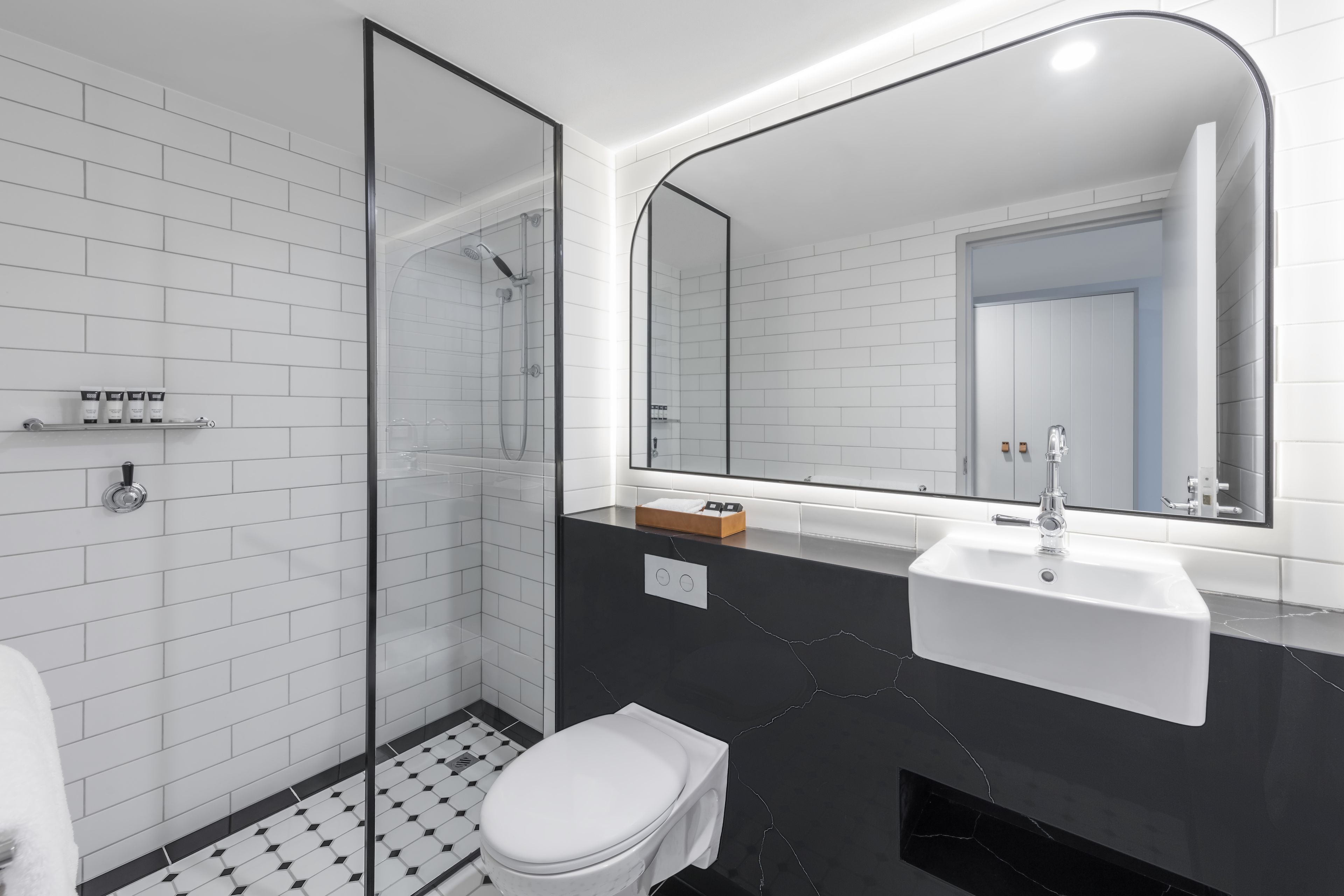Un baño moderno con ducha de vidrio, inodoro blanco y lavamanos de mármol negro.