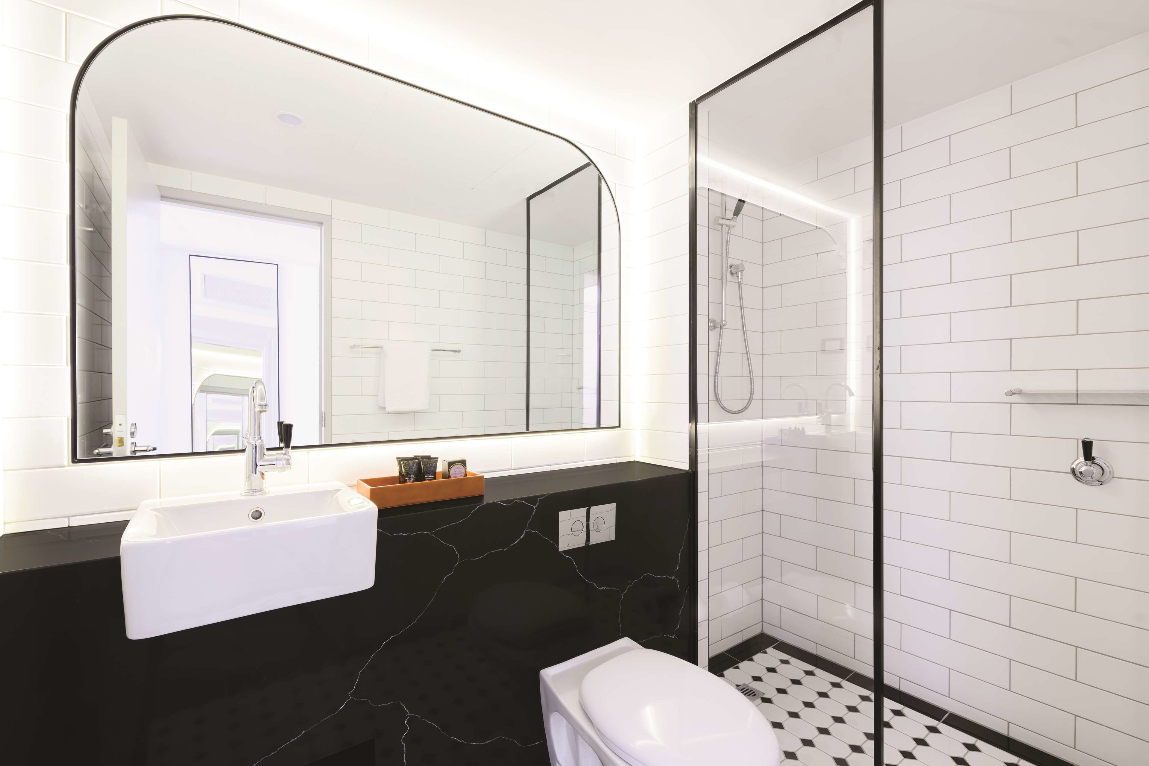 Un baño moderno con un lavamanos blanco, encimera negra y un espejo grande.