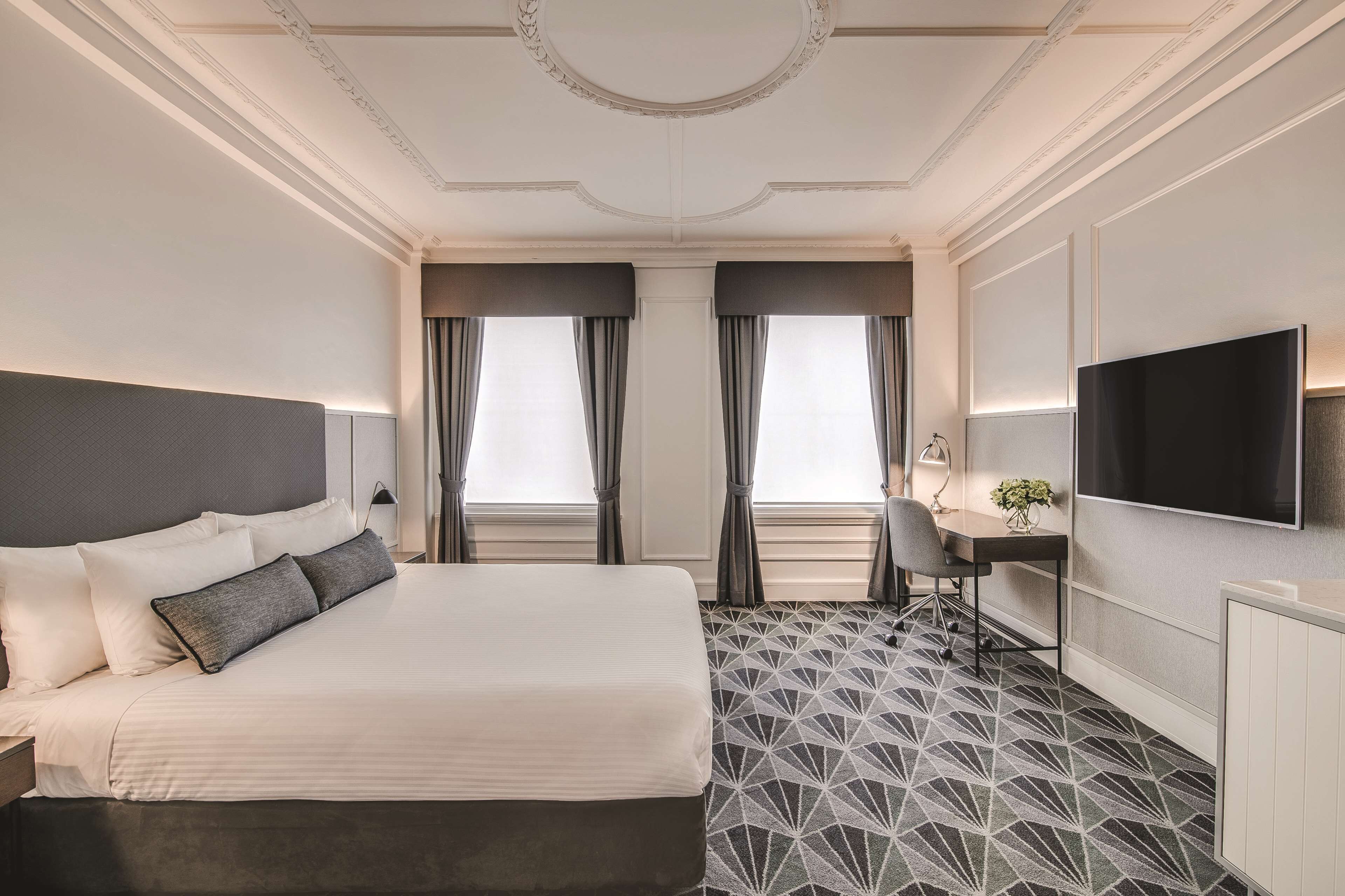 Habitación de hotel con una cama grande, un escritorio, una silla, un televisor y un piso con estampado.