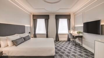 A hotel room with a large bed, a desk, a chair, a TV, and a patterned floor.