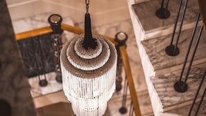 Ein Kronleuchter hängt über einer Treppe mit Marmorstufen und Metallgeländern.
