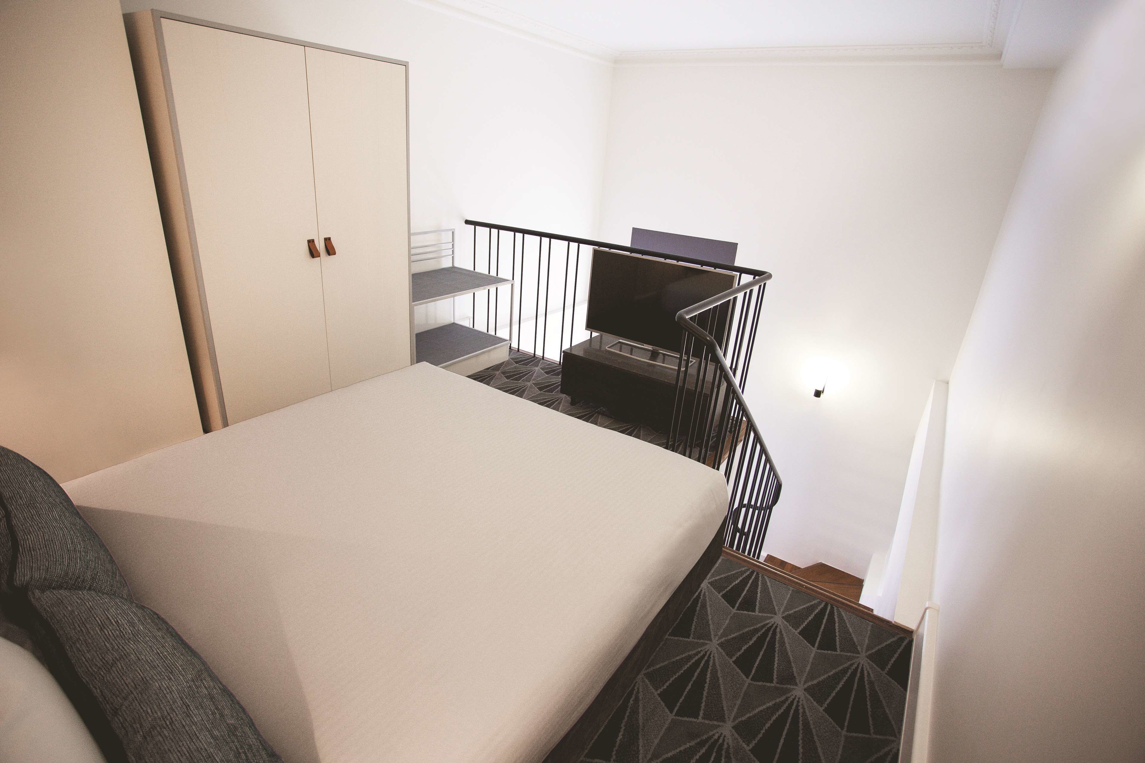 Un dormitorio con cama, armario, televisor y escalera.