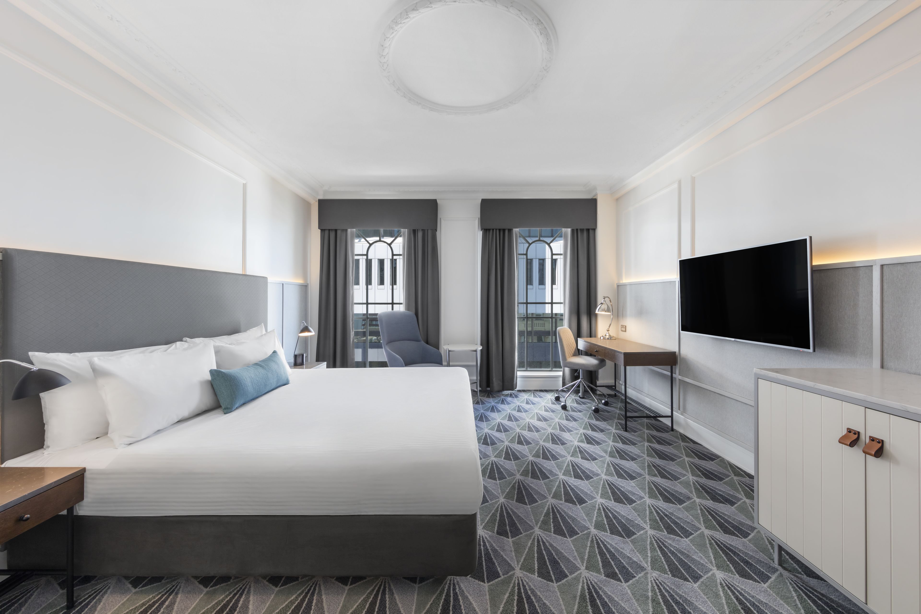 A modern hotel room with a large bed, a desk, a chair, and a TV.