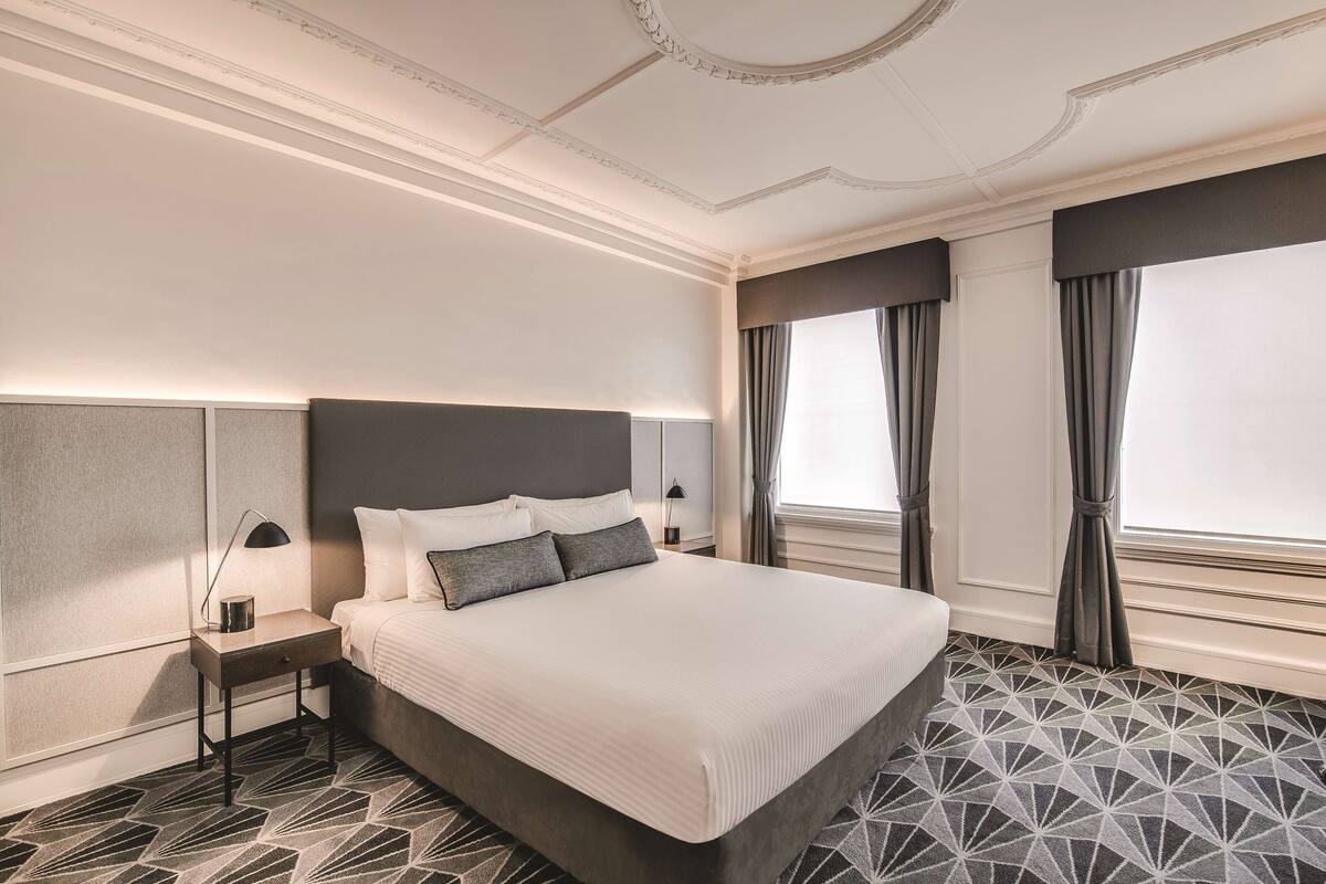 Ein Hotelzimmer mit einem großen Bett, einem Nachttisch mit Lampe und einem Teppich mit geometrischem Muster.