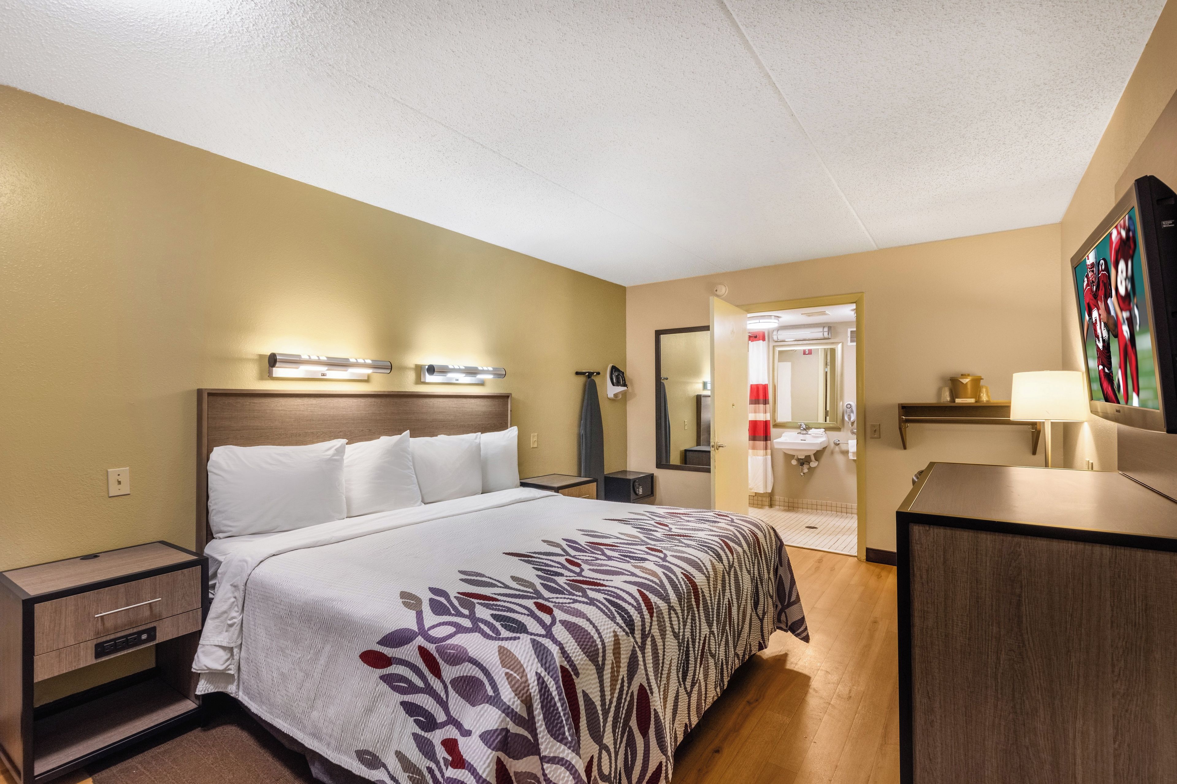 A hotel room with a bed, bedside tables, a desk, a mirror, and a television.