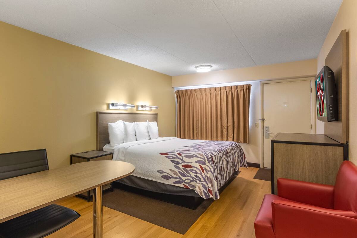 Ein Hotelzimmer mit Bett, Schreibtisch, Stuhl, Fernseher und einer Tür.