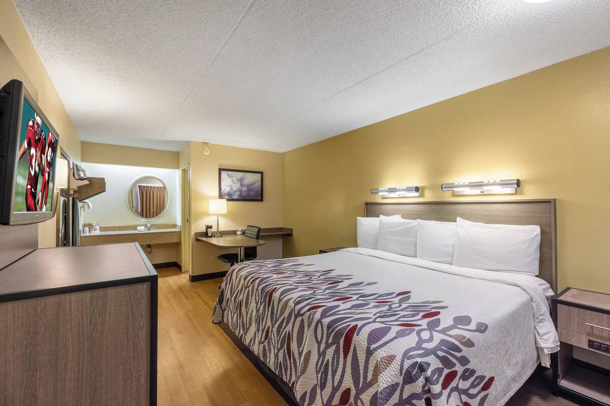 Ein Hotelzimmer mit einem großen Bett, einem Schreibtisch, einem Sessel, einem Fernseher und einem Badezimmer.