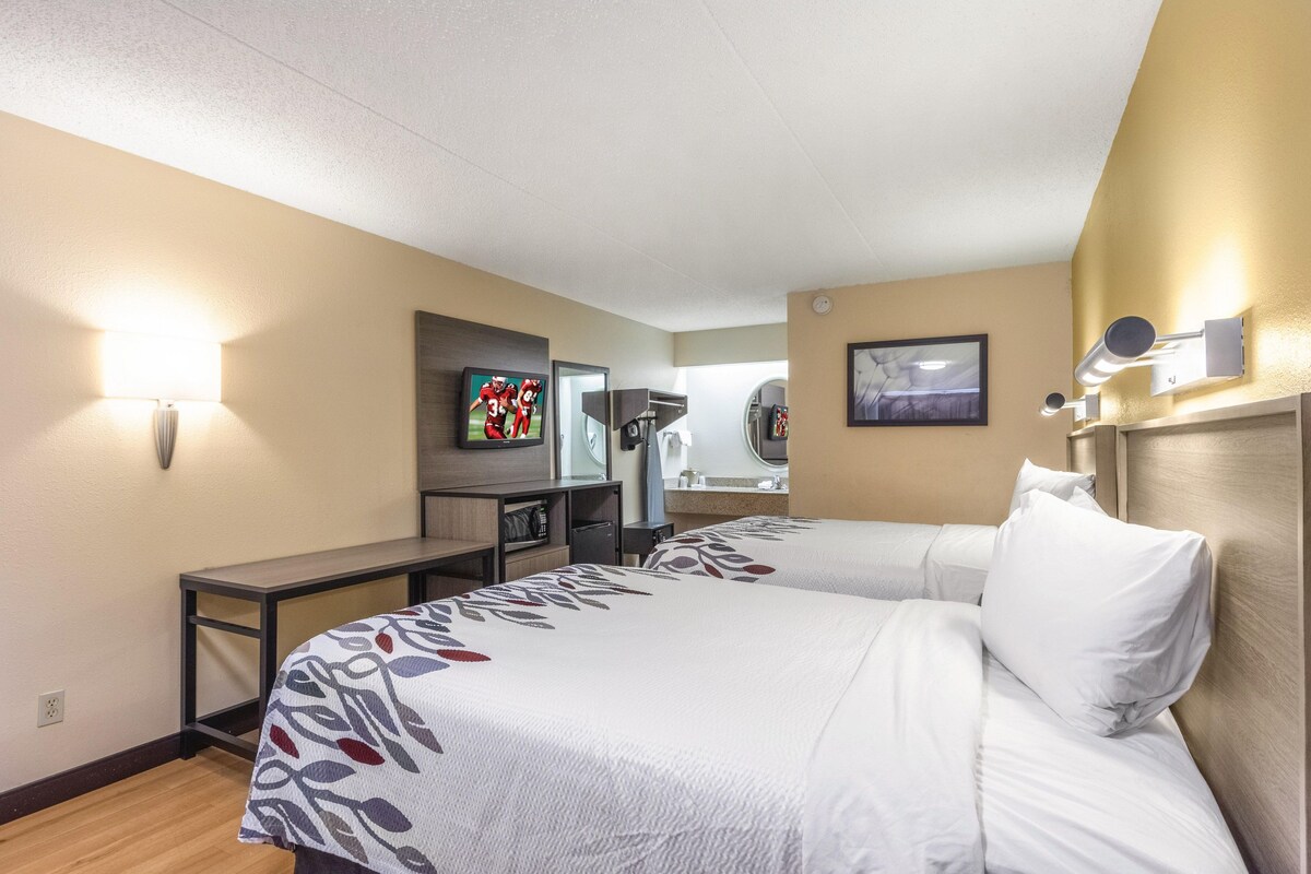 A hotel room with two beds, a desk, a TV, and a mirror.