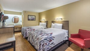 Ein Hotelzimmer mit zwei Betten, einem Schreibtisch, einem Stuhl und einem durch eine Tür einsehbaren Badezimmer.