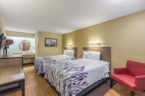 Une chambre d’hôtel avec deux lits, un bureau, une chaise et une salle de bain visible à travers une porte.