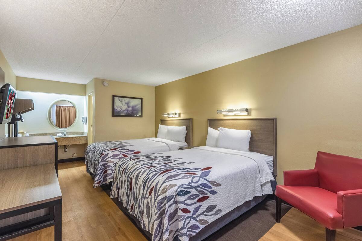 Ein Hotelzimmer mit zwei Betten, einem Schreibtisch, einem Stuhl, einem Spiegel und einem Bild an der Wand.