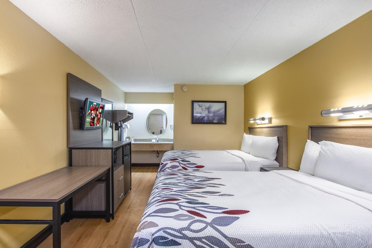 A hotel room with two beds, a desk, a TV, a mirror, and a painting on the wall.