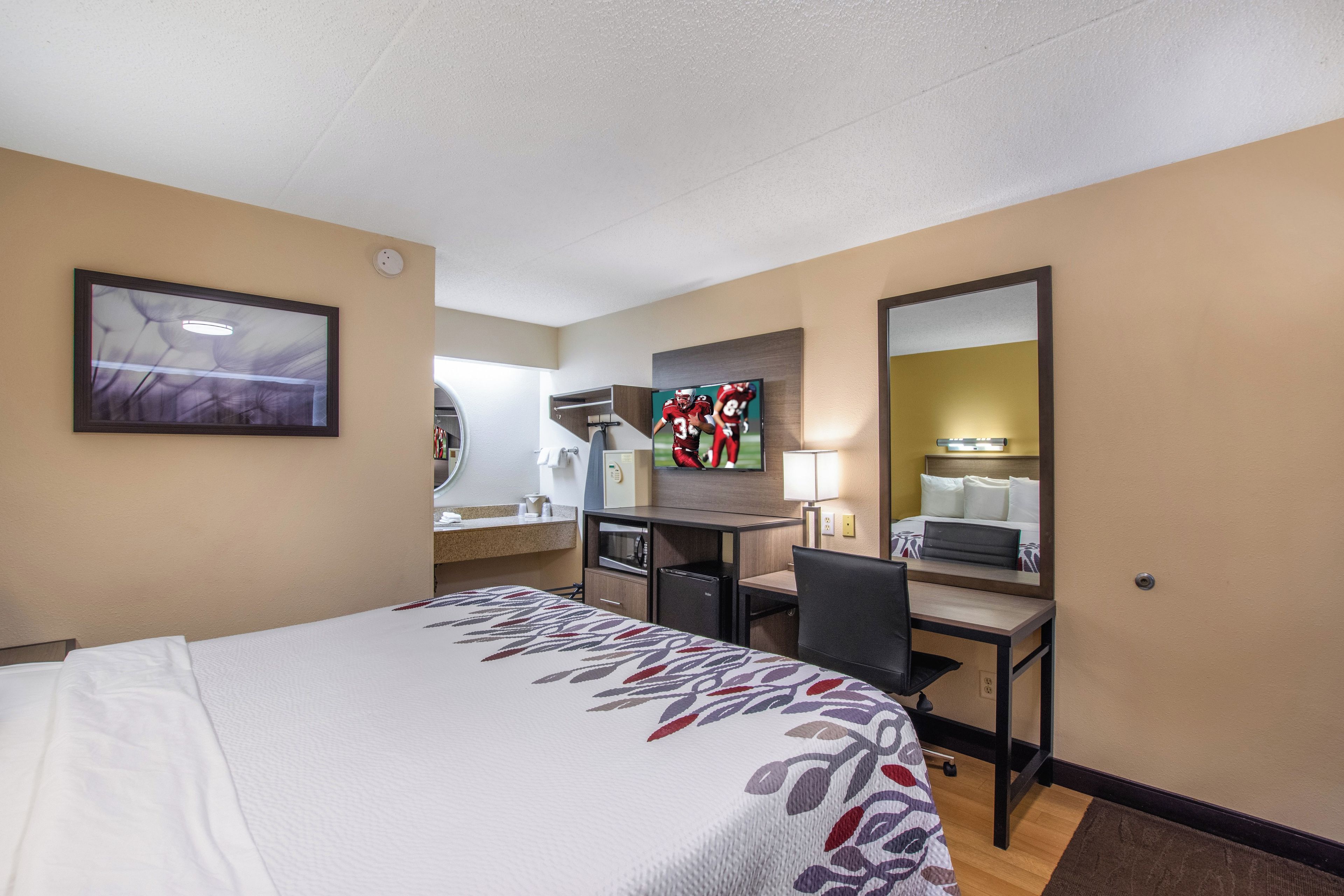 Une chambre d’hôtel équipée d’un lit, d’un bureau, d’une chaise, d’une télévision et d’un miroir.
