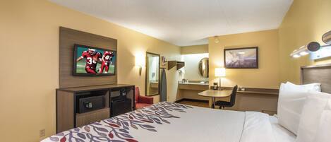 Habitación de hotel con cama, escritorio, silla, televisor, espejo y una caja de seguridad pequeña.
