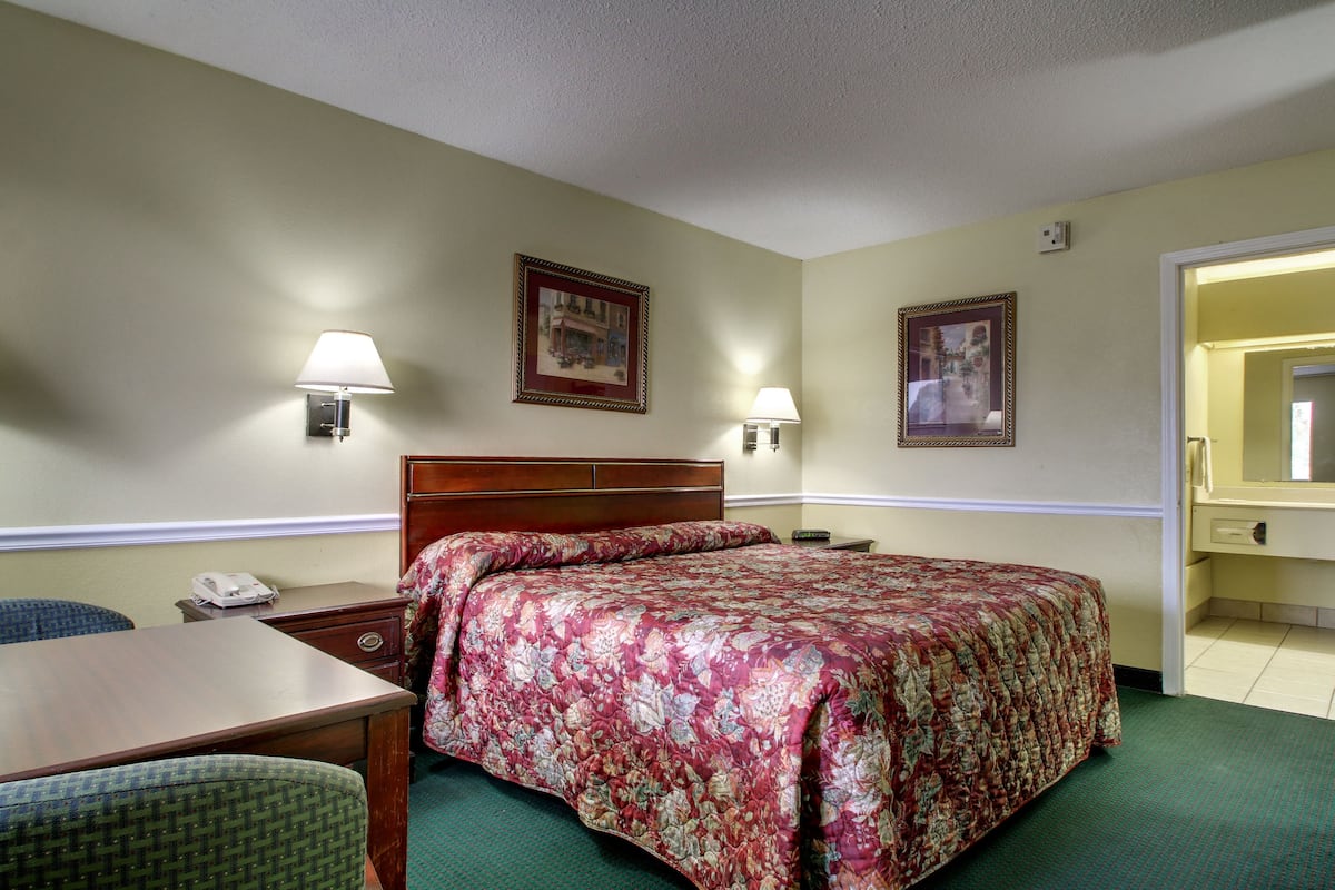Quarto de hotel com uma cama, duas luminárias de cabeceira, uma mesa com telefone e uma cadeira.
