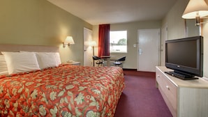 A hotel room with a large bed, a desk with a chair, a television, and a window with curtains. - Key West Inn - Montgomery (Montgomery)
